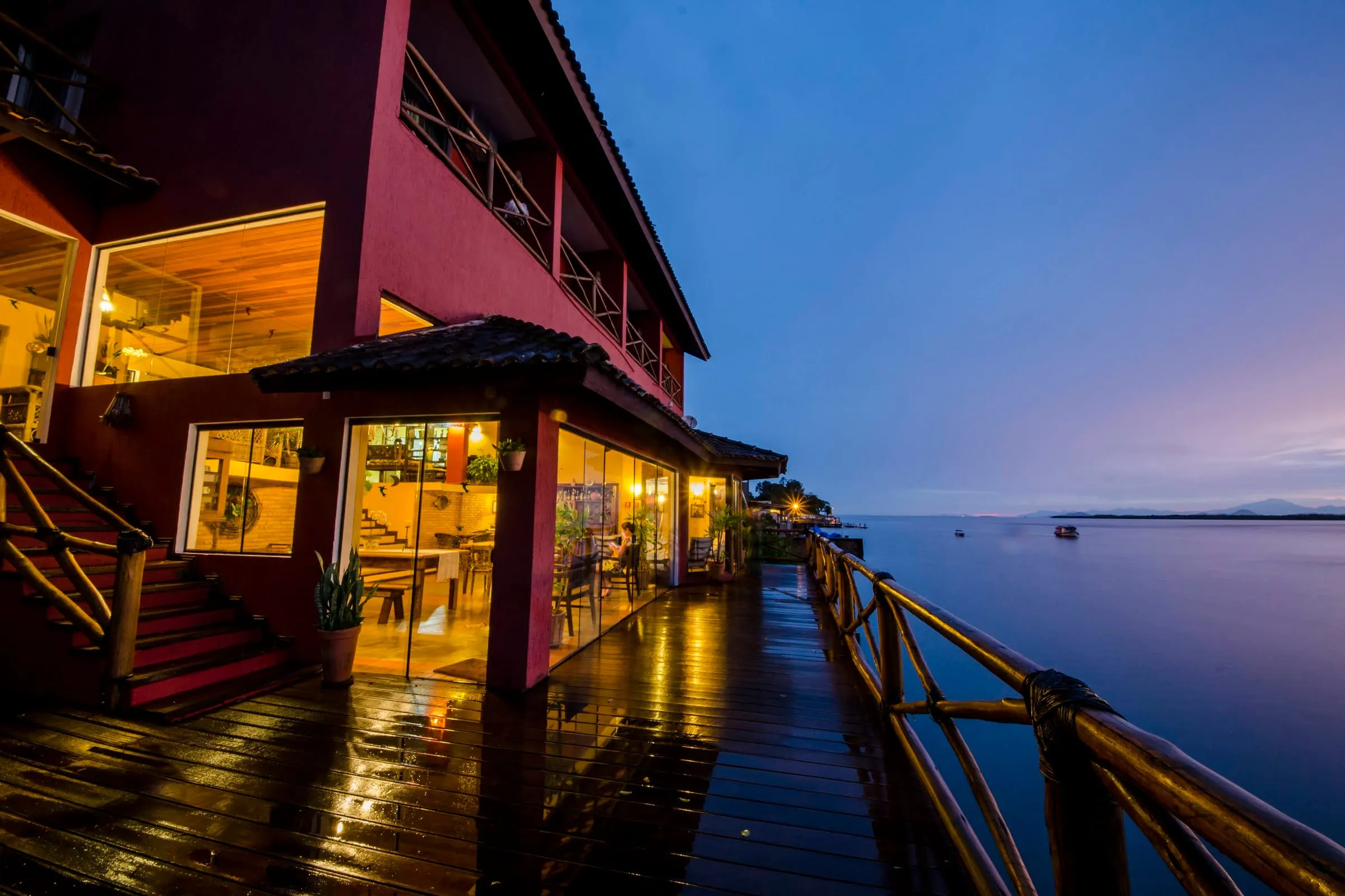 Fachada ao entardecer com o deck iluminado sobre a água