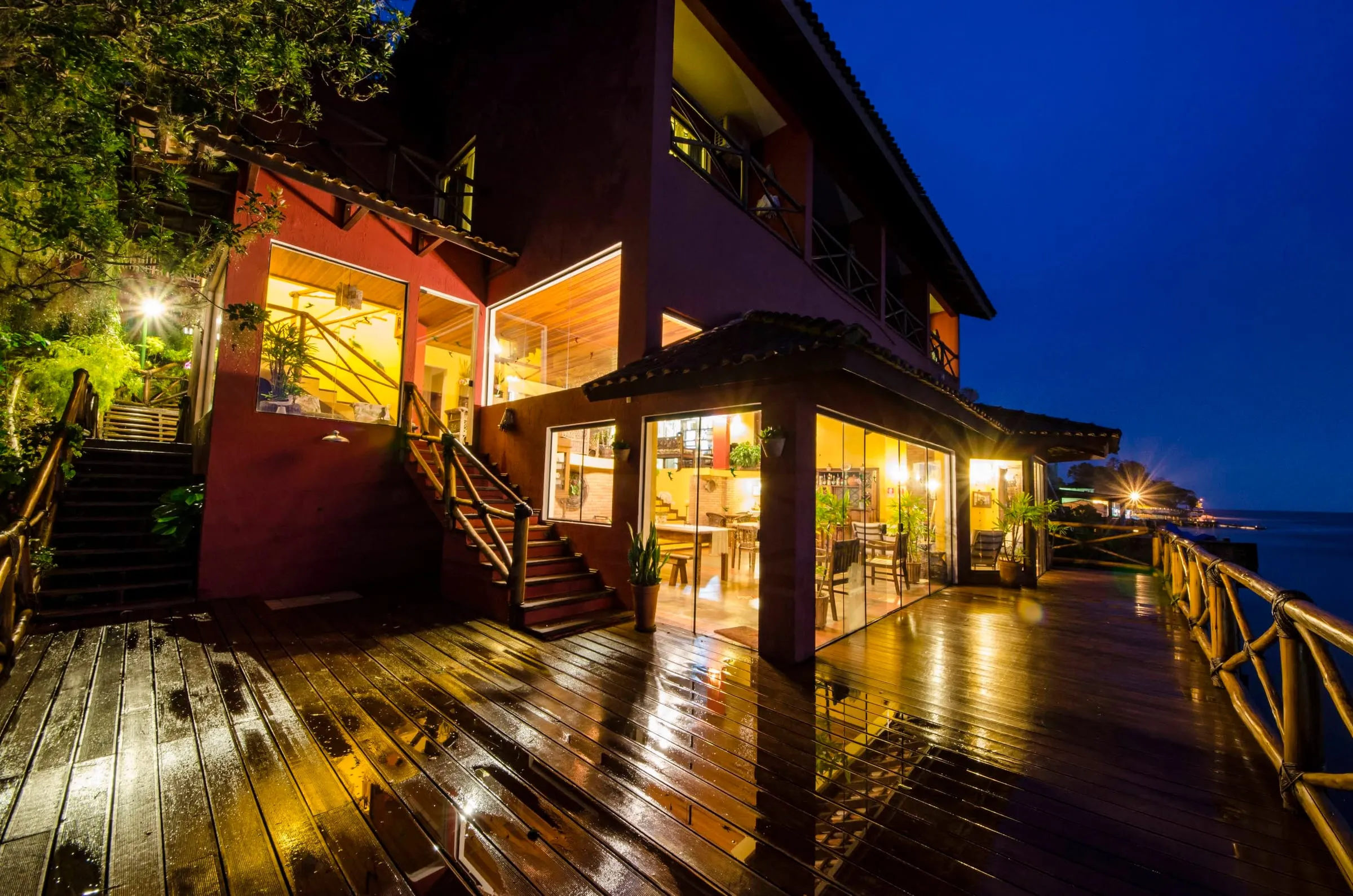 Fachada da pousada à noite, deck molhado refletindo as luzes
