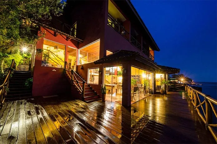 Fachada da pousada à noite, deck molhado refletindo as luzes