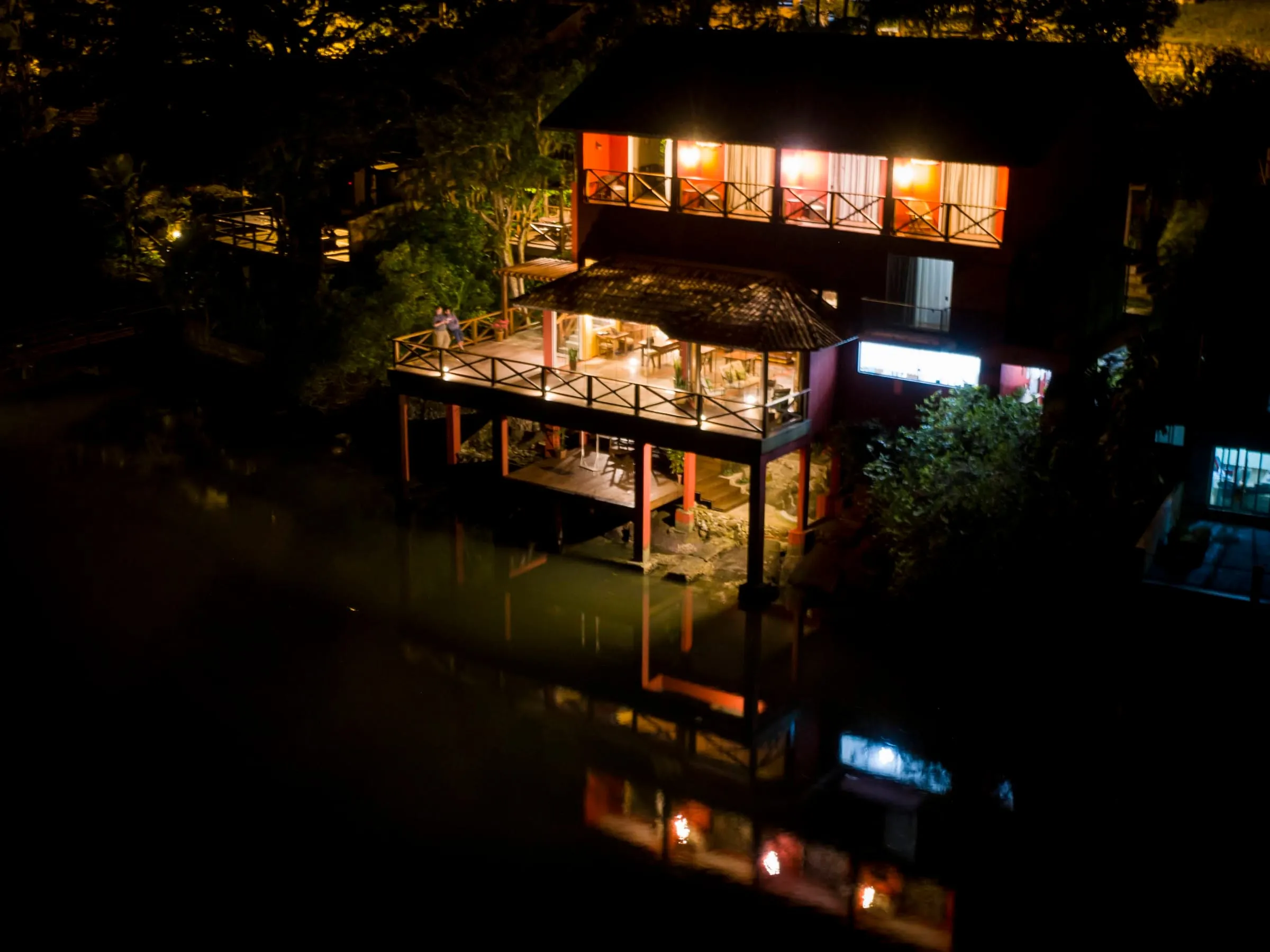 Vista aérea noturna da pousada iluminada, refletida na água