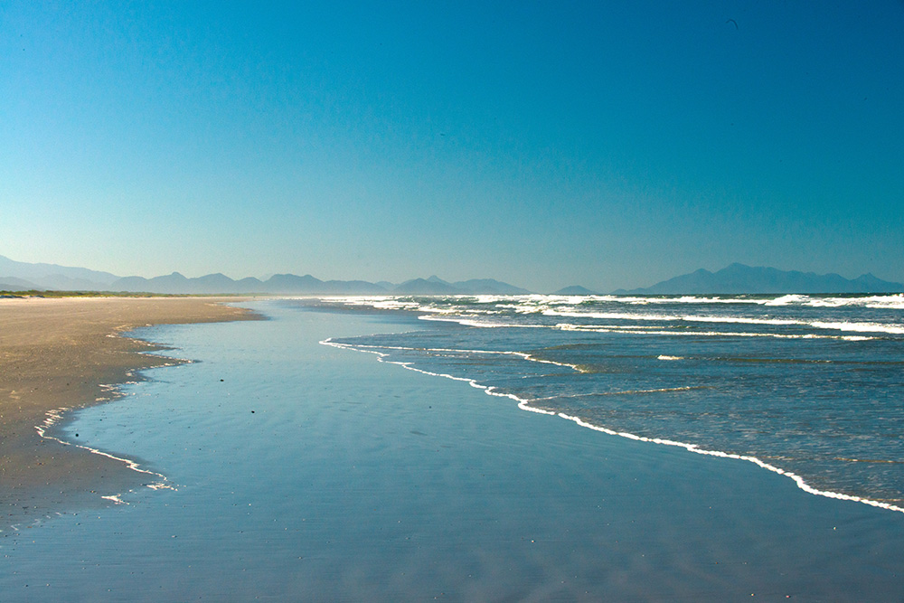 Praia deserta com águas claras e céu azul no Parque Nacional do Superagui